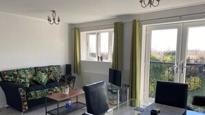 Uma sala de estar moderna com sofá, mesa de centro de vidro, televisão e varanda com cortinas.