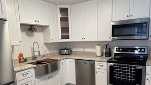 Uma cozinha moderna com armários brancos, eletrodomésticos de aço inoxidável, lava-louças, fogão e micro-ondas.