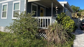 Uma casa térrea com varanda, o número '305' visível na lateral e um pequeno jardim com diversas plantas.