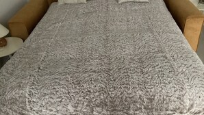 Una cama con un edredón texturizado, dos almohadas y un cabecero de madera.