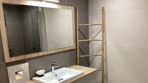Un baño con tocador de madera, un lavamanos blanco, un espejo y una escalera de bambú.