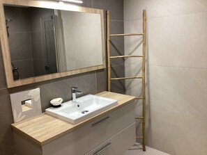 A bathroom with a wooden vanity, a white sink, a mirror, and a bamboo ladder.