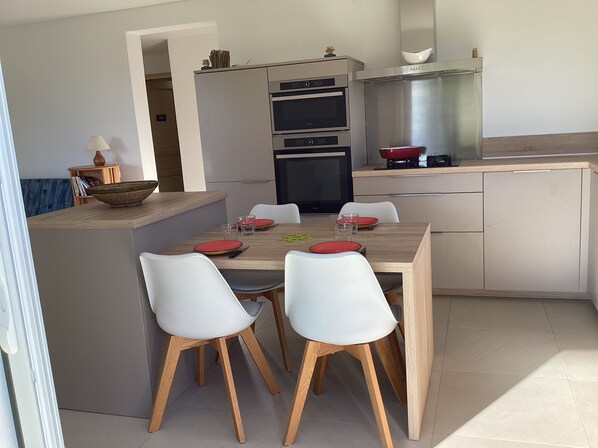 A modern kitchen with a central island, white chairs, and a dining table set for four.