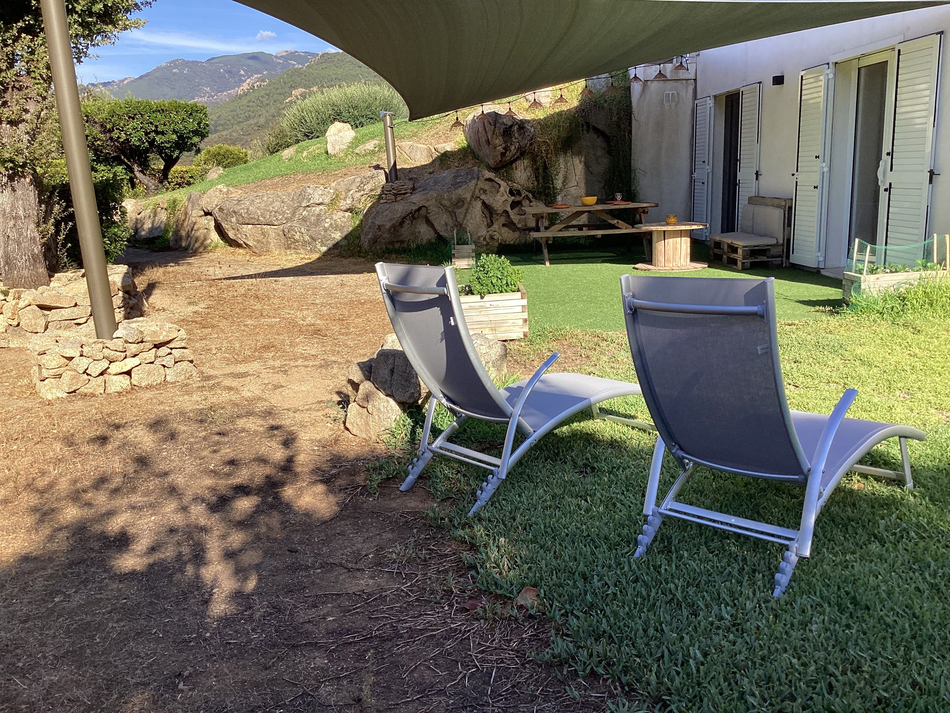 A patio area with two lounge chairs, a table with a bowl and a bottle, and a view of a mountainous landscape.