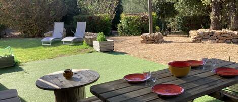 An outdoor patio with a wooden table set for dining, surrounded by green artificial grass, and a stone wall in the background.