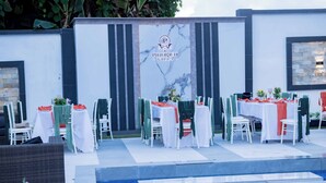 An outdoor dining area with tables set for a meal, a pool, and a wall with the logo "PINORICH VILLA". - Pinorich Villa (Buea)