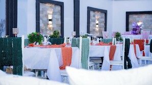 A restaurant with outdoor seating, white tables, and chairs with green and orange drapes. - Pinorich Villa (Buea)