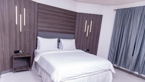 A modern bedroom with a large bed, wooden headboard, and a nightstand. - Pinorich Villa (Buea)