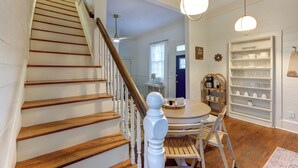 Un escalier avec des marches en bois et une rampe blanche, menant à une pièce où se trouvent une table à manger, des chaises et une table basse.