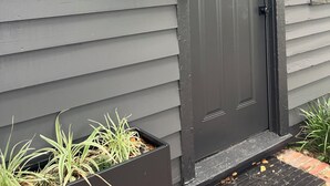 Une porte gris foncé, surmontée d’une petite fenêtre, avec une boîte aux lettres et un jardinier contenant des plantes à sa base.