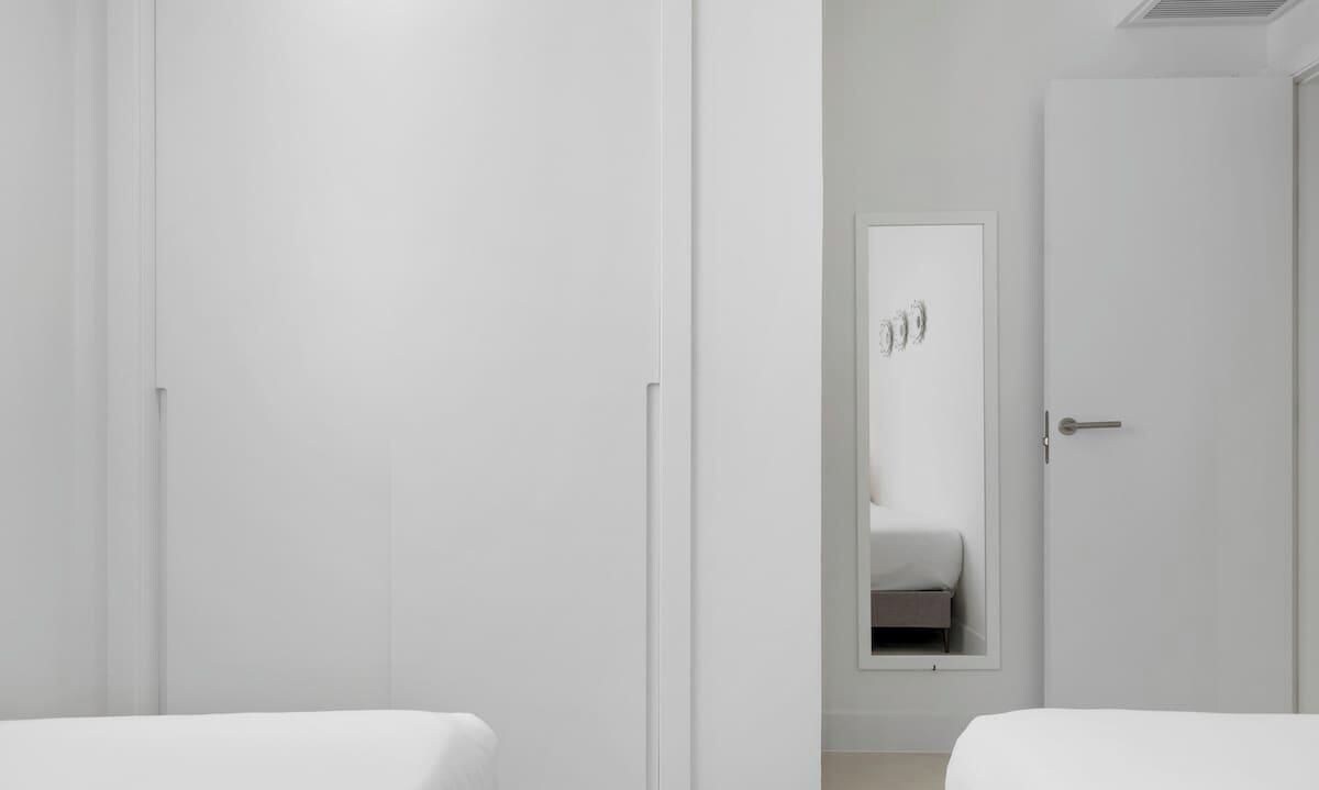 Habitación de hotel con dos camas, una puerta y un espejo que refleja una cama.