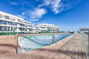 A modern hotel with a pool area, wooden deck, and balconies overlooking the pool.