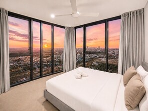 Een hotelkamer met een groot bed, een plafondventilator en uitzicht op de stad.