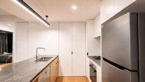 A modern kitchen with a marble countertop, stainless steel appliances, and wooden flooring. - City Lights Views – 2BR Stay (South Brisbane)