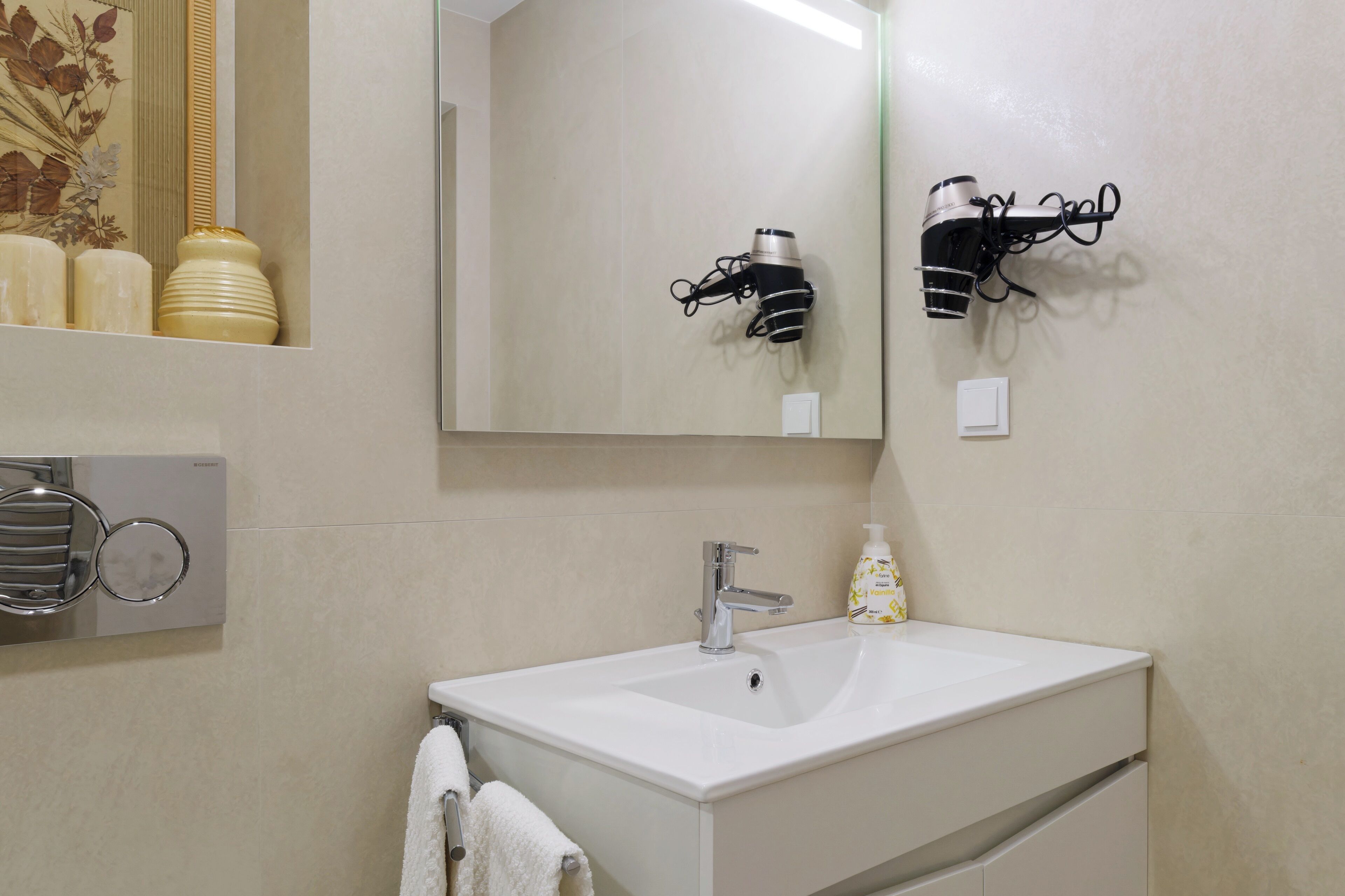 A bathroom with a white sink, a mirror, a towel rack, and a hairdryer mounted on the wall.
