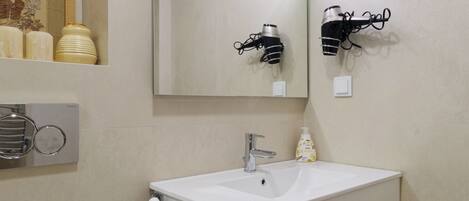 A bathroom with a white sink, a mirror, a towel rack, and a hairdryer mounted on the wall.