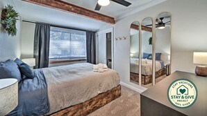 A bedroom with a bed, a ceiling fan, a window with blinds, a mirror, and a door leading to another room. - Flagstaff Forest Retreat • Hot Tub • Fire Pit • Fully Fenced Yard • P... (Flagstaff)
