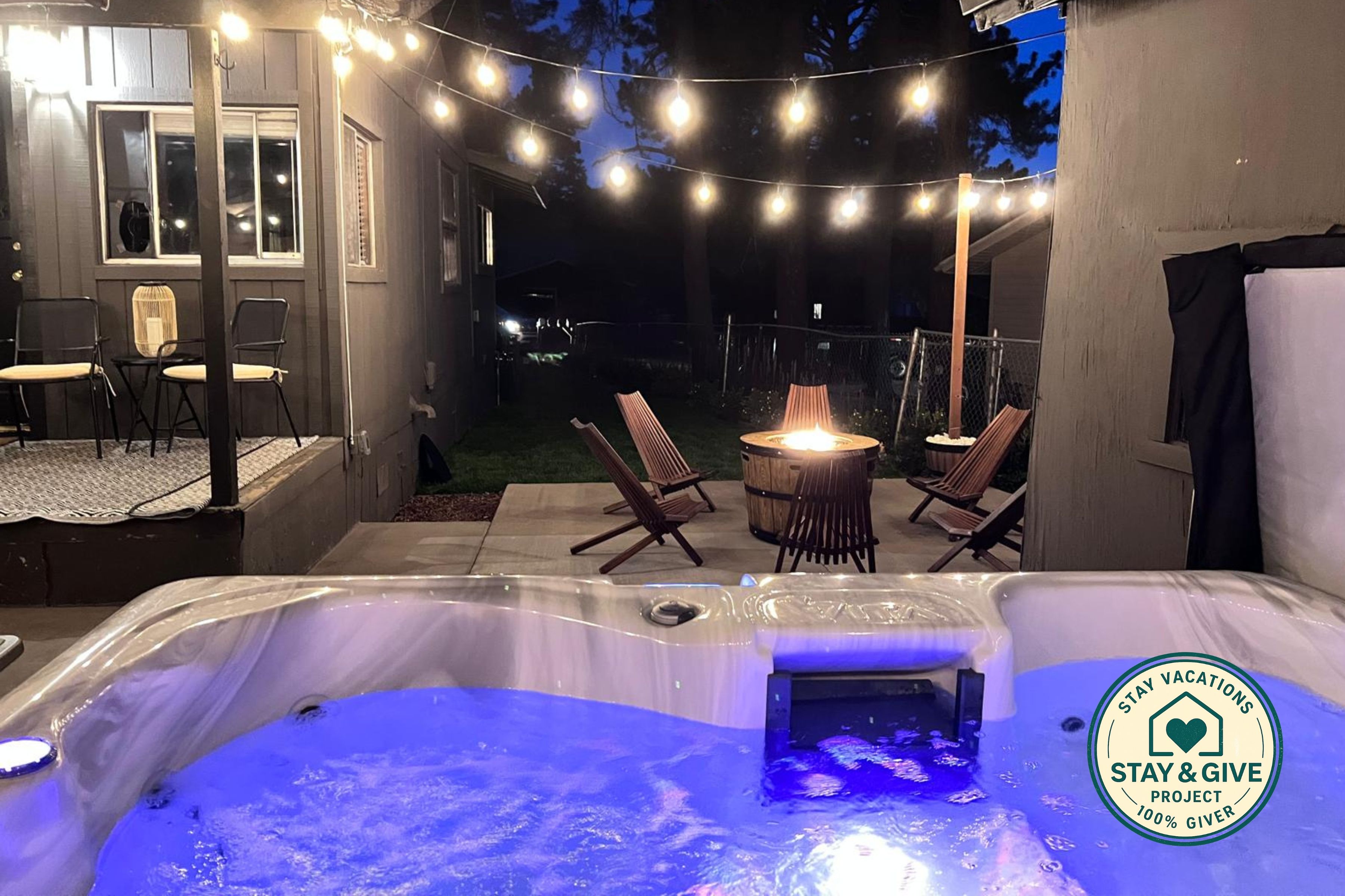 Ett utomhusområde med ett bubbelbad, ljusslingor, en eldstad och sittplatser.