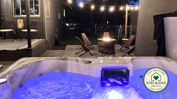 Ett utomhusområde med ett bubbelbad, ljusslingor, en eldstad och sittplatser.