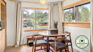 A room with a round wooden table, four chairs, a potted plant, and a window with a view of trees and a vehicle outside. - Flagstaff Forest Retreat • Hot Tub • Fire Pit • Fully Fenced Yard • P... (Flagstaff)