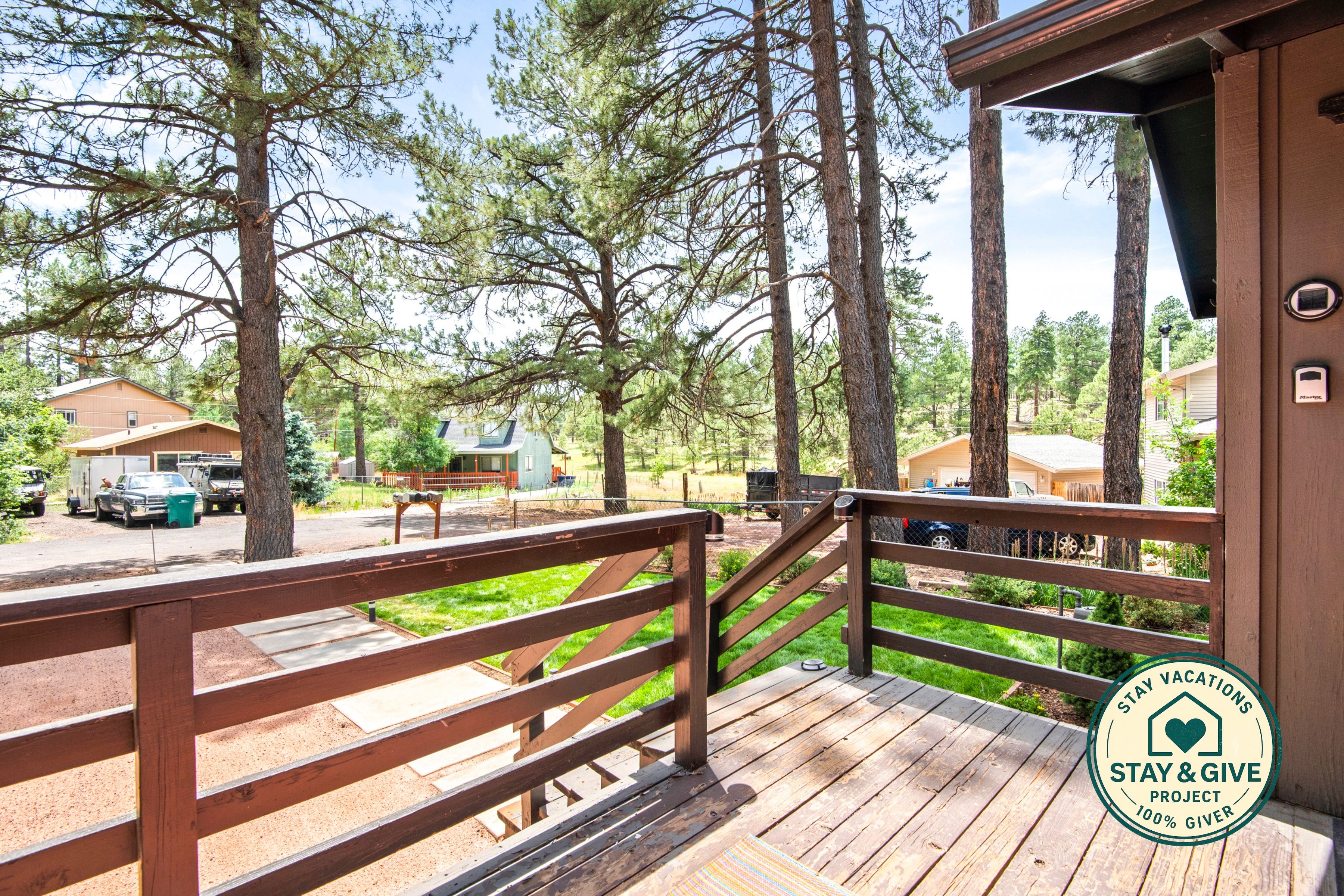 A wooden deck with a railing, overlooking a forested area with several cabins.