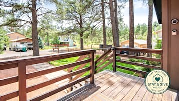 A wooden deck with a railing, overlooking a forested area with several cabins.