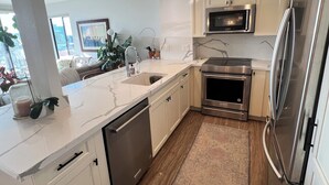 A modern kitchen with white cabinetry, stainless steel appliances, and a marble countertop. - Urban Oasis with Sweeping Views - Walk to Gaslamp, Little Italy, Balboa Park (San Diego)