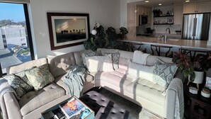 A modern living room with a sectional sofa, a coffee table, and a view of the city through a large window. - Urban Oasis with Sweeping Views - Walk to Gaslamp, Little Italy, Balboa Park (San Diego)
