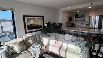 Un salon moderne avec un canapé d’angle, une table basse et une vue sur la ville grâce à une grande fenêtre.