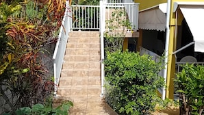 A yellow building with a staircase leading to a balcony, surrounded by greenery. - Top of Villa LA FLEUR DE CANNE (Lamentin)