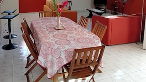 A dining area with a table set for six, surrounded by wooden chairs, in a room with a sloped ceiling and a red accent wall. - Top of Villa LA FLEUR DE CANNE (Lamentin)