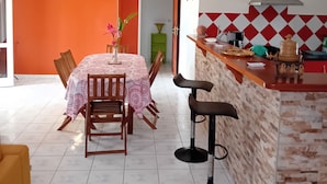 A dining area with a table and chairs, a kitchen with a counter and stools, and a ceiling fan. - Top of Villa LA FLEUR DE CANNE (Lamentin)