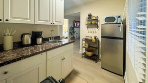 Una cocina con gabinetes blancos, encimera de granito, refrigerador de acero inoxidable, microondas y cafetera.