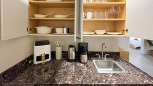 Cocina compacta con estantes empotrados que contienen vajilla y vasos, una cafetera y un hervidor.