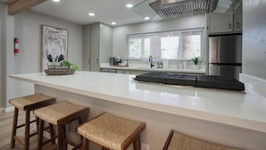 A modern kitchen with a large island, bar stools, stainless steel appliances, and a glass ceiling vent.