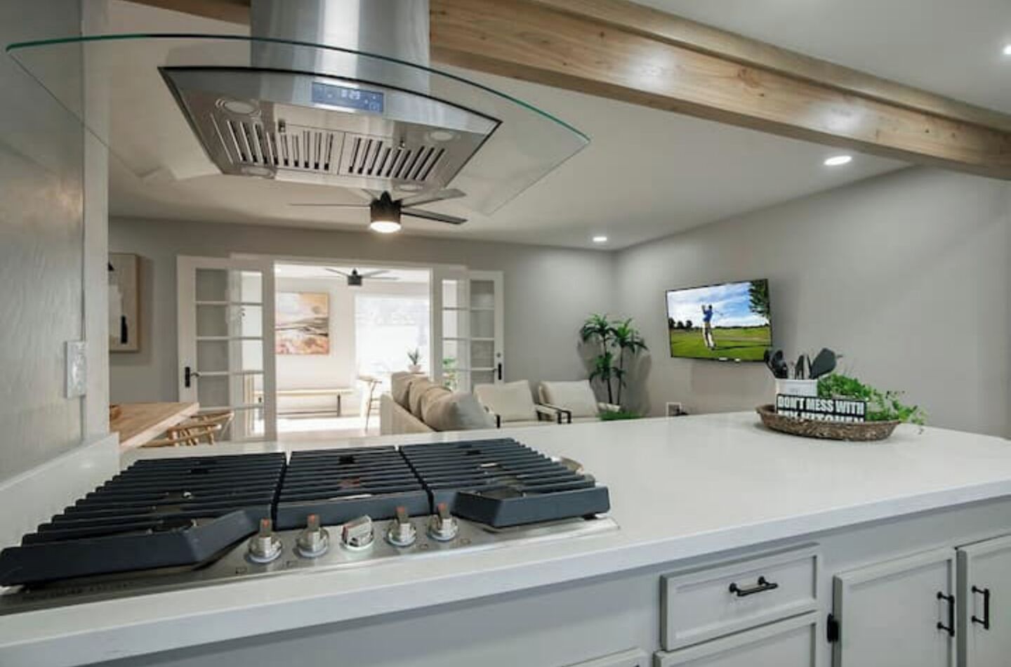 A modern kitchen with a gas stove, a ceiling fan, and a TV mounted on the wall.