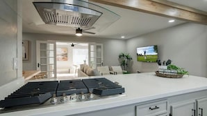 A modern kitchen with a gas stove, a ceiling fan, and a TV mounted on the wall.