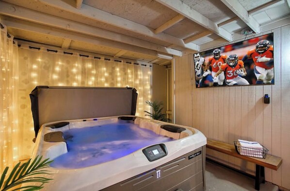 A hot tub with a control panel, a wooden bench, and a wall-mounted TV displaying sports players. - Walk to Old Town! Hot Tub • Game Room • Glow Golf • Pet Friendly • Sl... (Scottsdale)