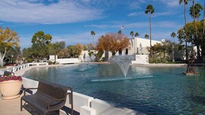 A pool with a water feature, surrounded by palm trees and a white building.