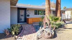 A modern house with a brick pathway leading to a wooden bench and a cactus garden.