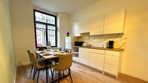 A modern kitchen with a dining table set for four, wooden flooring, white cabinets, and a marble backsplash. - Family-friendly vacation apartment with parking space (Leipzig)