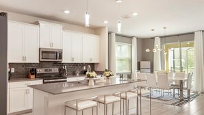 A modern kitchen with white cabinets, stainless steel appliances, and a central island with bar stools. - Amazing 7 BR STOREY LAKE RESORT, ideal location, close to everything 2801 (kissimmee)