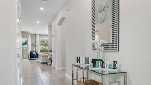 A modern hallway with a glass console table displaying 'HOME' and 'WELCOME' signs, a woven basket, and a decorative mirror with fish patterns. - Amazing 7 BR STOREY LAKE RESORT, ideal location, close to everything 2801 (kissimmee)