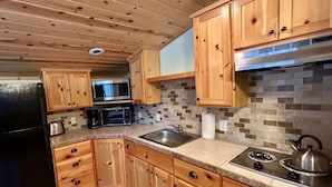 Una cocina con armarios de madera, microondas, estufa y pileta.