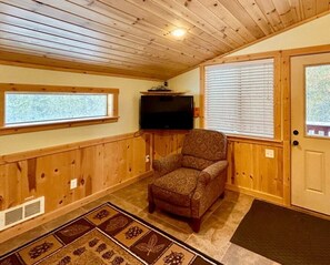 A wooden-paneled room with a television, a patterned rug, and a door with a window. - Trailer Parking- Dogs Welcome-Play and Fun (Island Park)