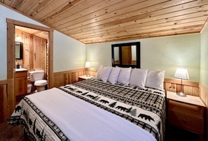 A wooden-paneled room with a bed, bedside tables, a mirror, and a toilet.