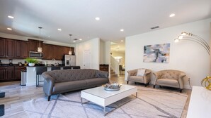 A modern living room with a sofa, coffee table, and a kitchen in the background. - 421 NP - Exquisite Retreat at Encore Resort (Kissimmee)