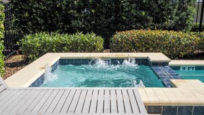 A hot tub surrounded by a wooden deck and a tiled pool area, with lush greenery in the background. - 421 NP - Exquisite Retreat at Encore Resort (Kissimmee)
