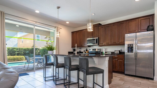 A modern kitchen with a large island, stainless steel appliances, and a sliding glass door leading to a patio area. - 421 NP - Exquisite Retreat at Encore Resort (Kissimmee)