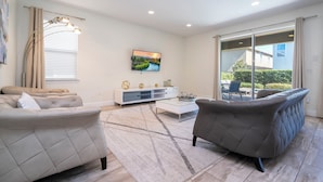 A modern living room with a sofa, armchair, and coffee table, a flat-screen TV, and a sliding glass door to the outside. - 421 NP - Exquisite Retreat at Encore Resort (Kissimmee)